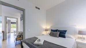 A modern hotel room with a large bed, a bedside table with a lamp, a chair, and a view of the outdoors. - Almería, Suite 344, Aralia (Vera)