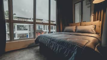 A bedroom with a large window, a bed with a headboard, and a view of buildings outside.