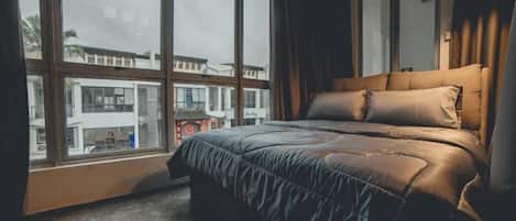 A bedroom with a large window, a bed with a headboard, and a view of buildings outside.