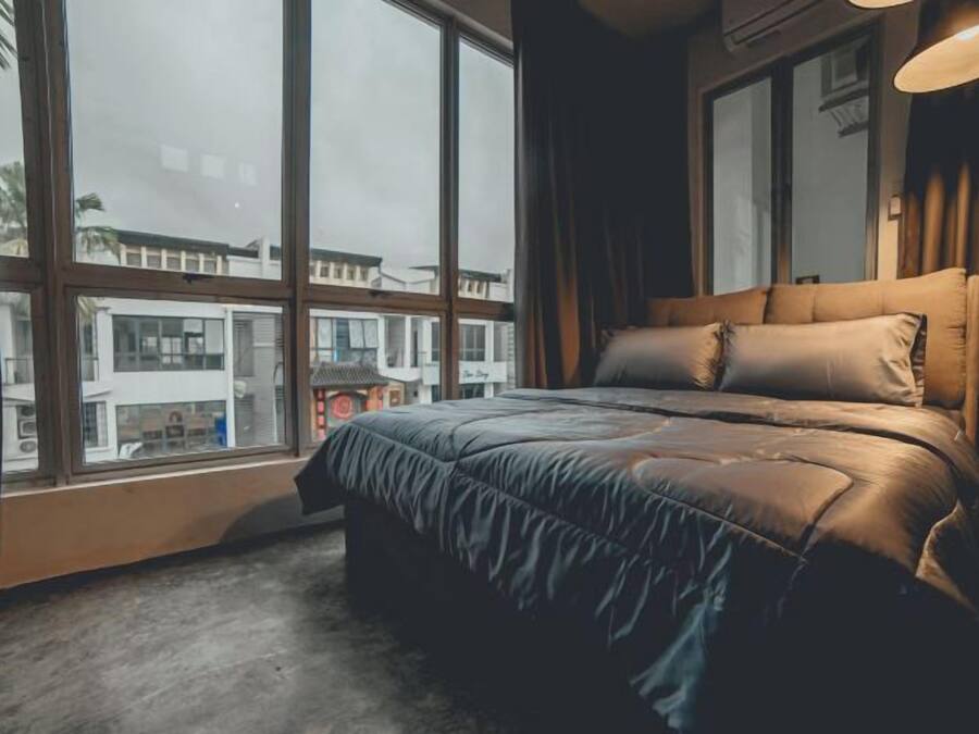 A bedroom with a large window, a bed with a headboard, and a view of buildings outside.