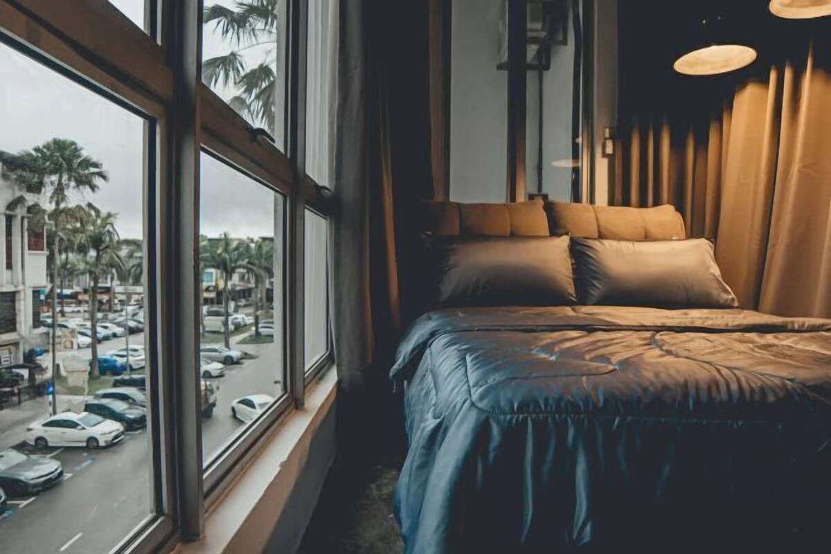 A bedroom with a large window, a bed with a blue cover, and a view of palm trees and parked cars outside.