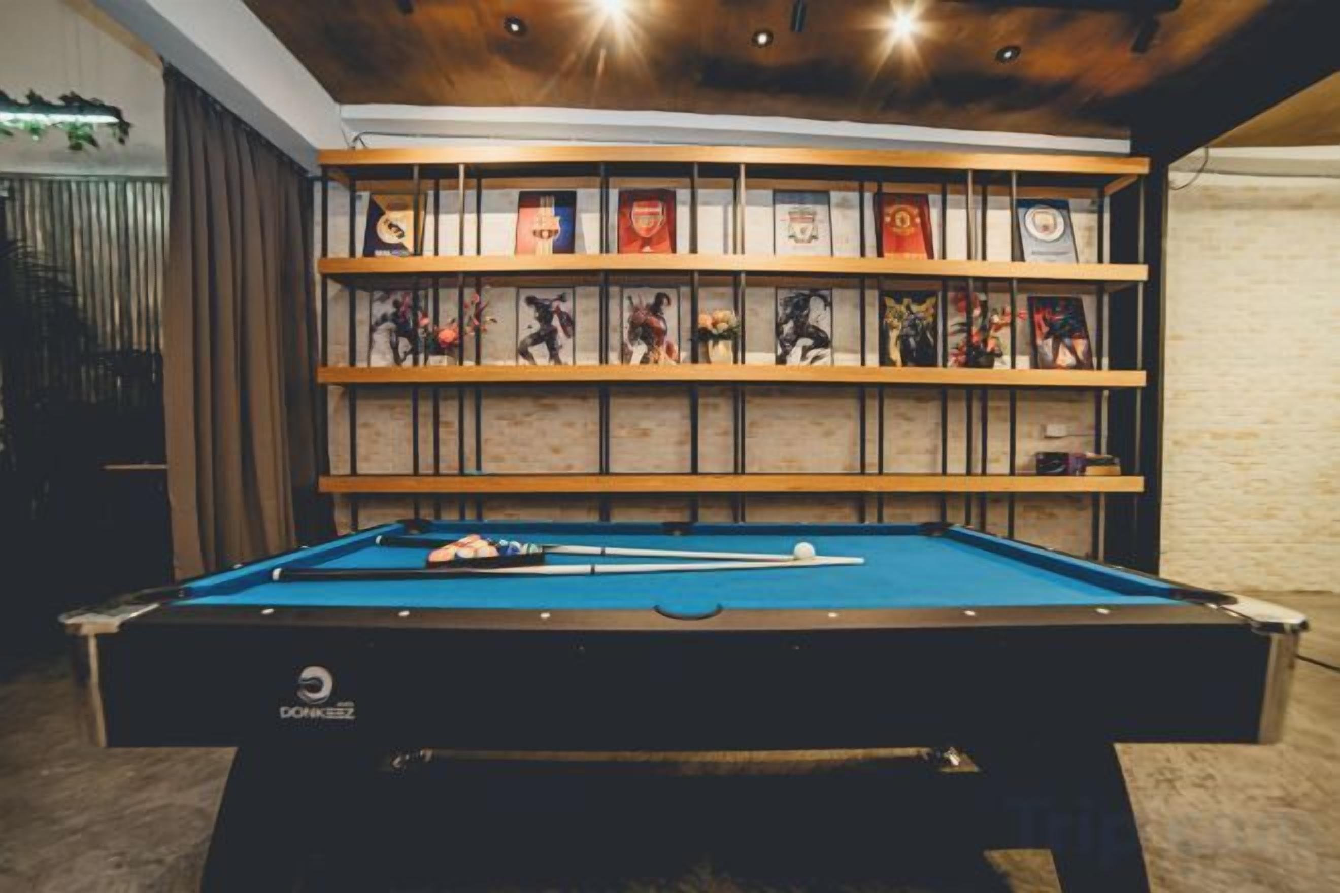 A pool table with a blue felt surface, surrounded by shelves with framed pictures and trophies.