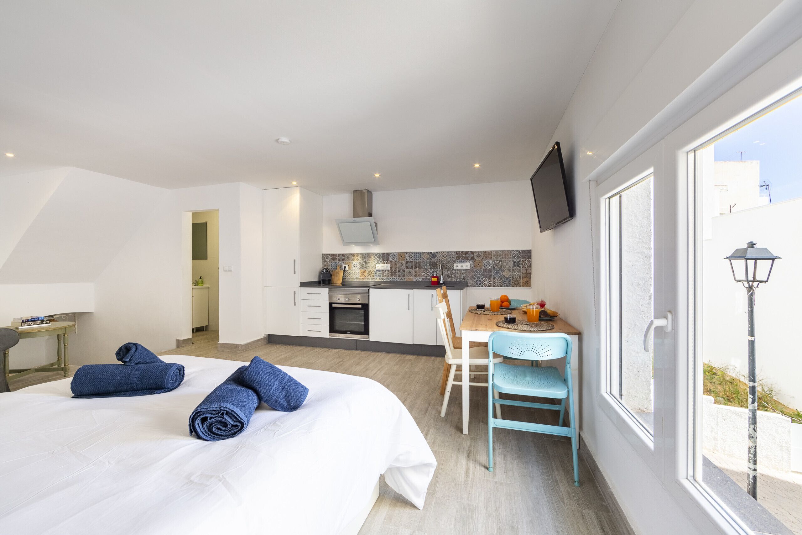 Quarto de hotel com cama, escrivaninha, cadeira, televisão e janela.