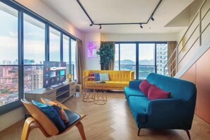 A modern living room with a large window, a yellow sofa, a blue sofa, a TV, and a plant.