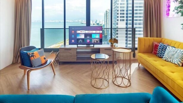 A modern living room with a large TV, a yellow sofa, and a view of the city. - Sunrise Gurney (George Town)