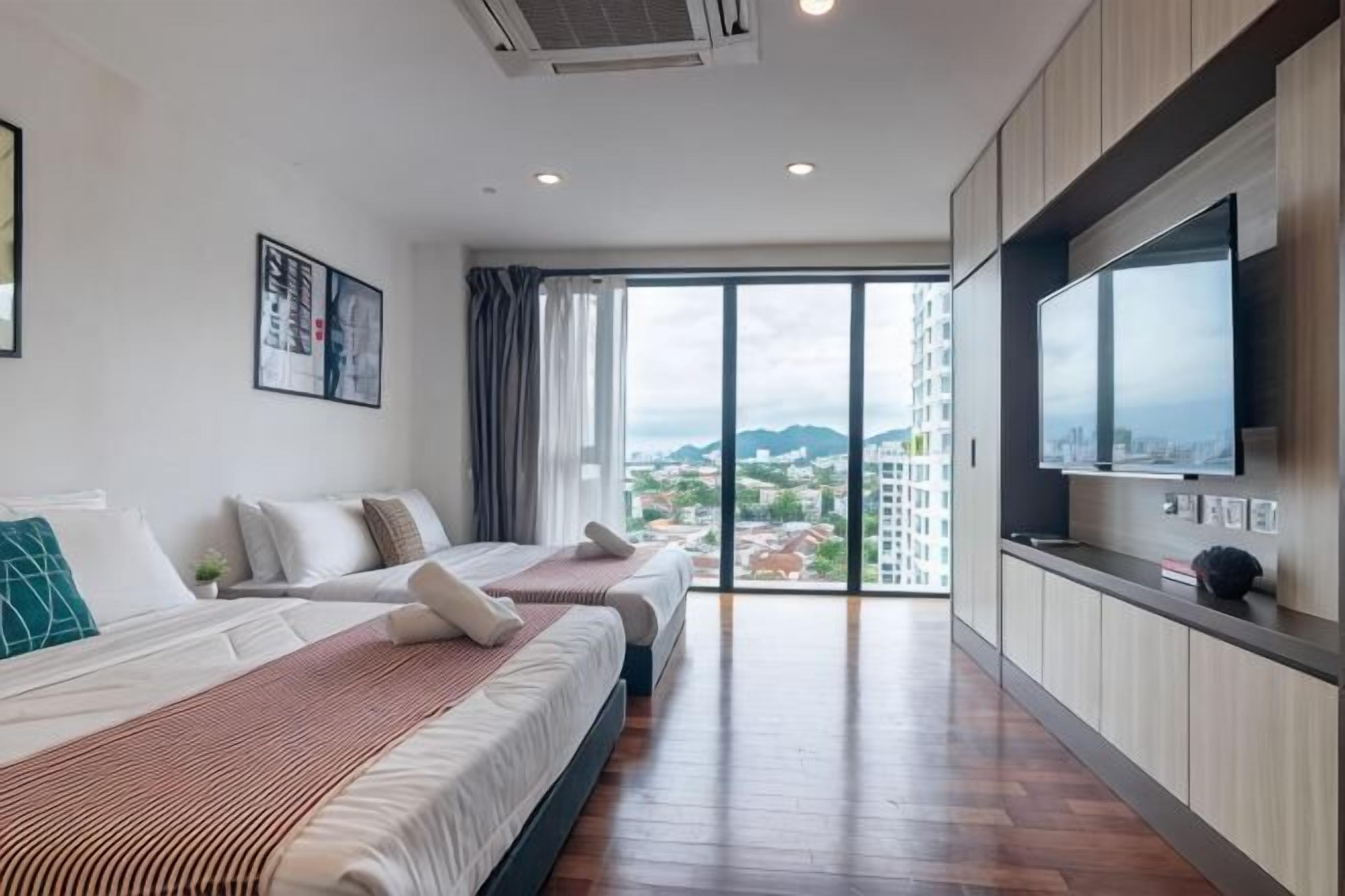 Habitación de hotel moderna con dos camas, un televisor grande y vista a la ciudad.