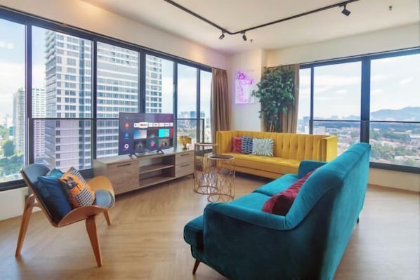 A modern living room with a large window, a yellow sofa, a teal sofa, and a wooden chair. - Sunrise Gurney (George Town)