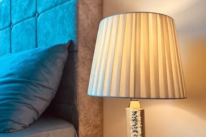 Een lamp met een plooilamp en een gestreept voetje, naast een kussen op een bank.