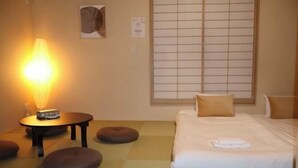 A hotel room with a bed, pillows, a table with a lamp, and a window with blinds.