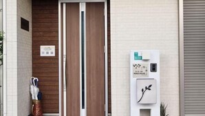A hotel entrance with a wooden door, a signboard with room numbers, and a small plant on the wall.