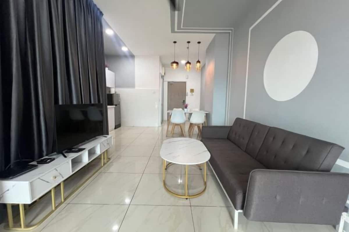 A modern living room with a sofa, a TV, a dining area with chairs, and a kitchen in the background.