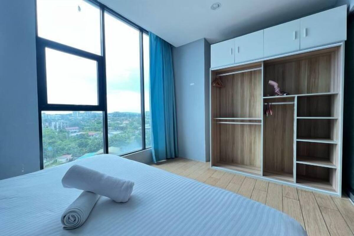 A hotel room with a large window, a bed with a rolled towel, and a wardrobe with multiple shelves.