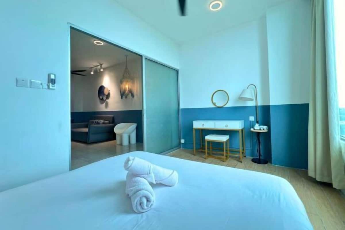 A hotel room with a bed, a desk, a chair, a lamp, and a view of the bathroom.
