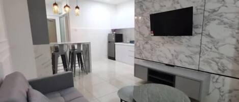 Una sala de estar moderna con un sofá gris, una mesa redonda y un televisor montado en una pared de mármol.
