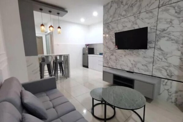 A modern living room with a grey sofa, a round table, and a TV mounted on a marble wall.