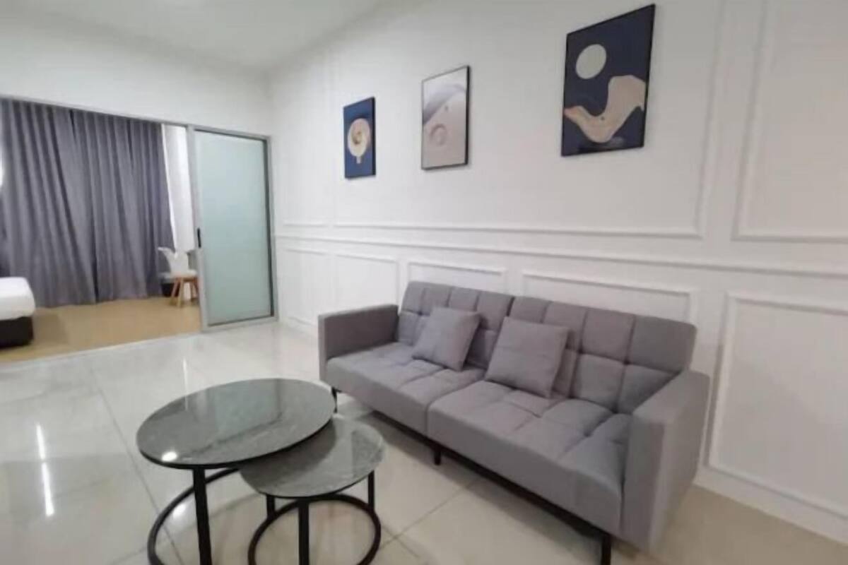 A modern living room with a grey sofa, a glass coffee table, and three framed artworks on the wall.