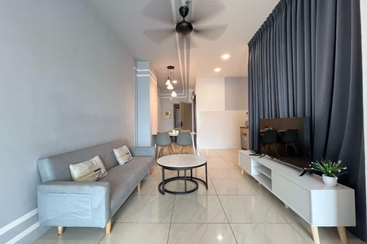 A modern living room with a sofa, a round coffee table, a TV, and a dining area in the background.