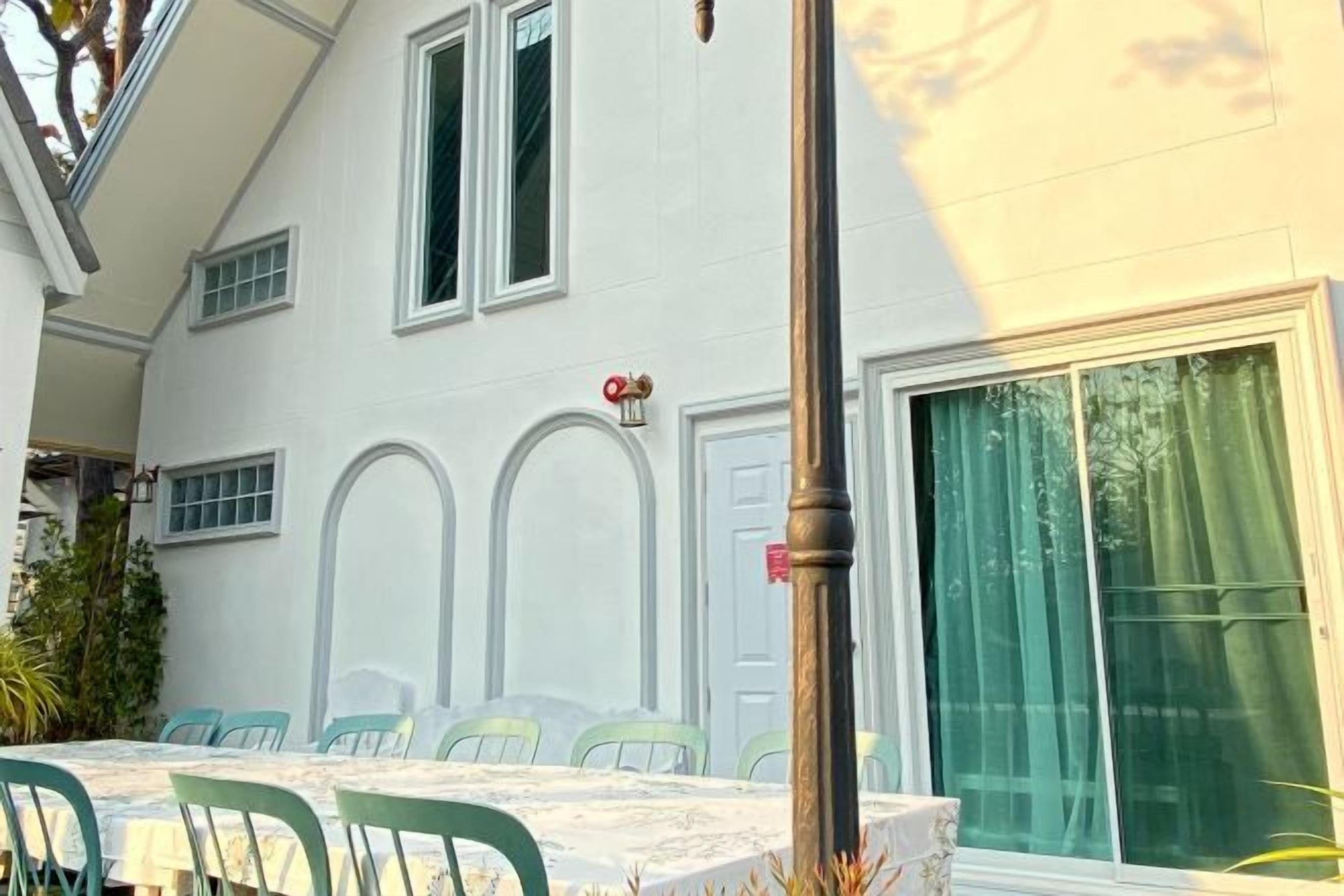 Un espace repas avec une table et des chaises, un bâtiment doté de fenêtres en arc de cercle et une porte avec une enseigne rouge.