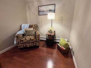A living room with a patterned armchair, a small table with a lamp, and a basket with items. - Spacious Townhouse l Retreat on Pawtuckaway River (Nottingham)