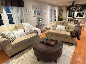 A living room with two beige sofas, a brown ottoman, and a small table with a plant.