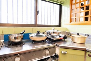 A kitchen with a gas stove, pots, and a window with blinds. - Agari (Ie)