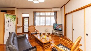 A living room with a sofa, chairs, a table, a television, and a traditional Japanese sliding door. - Agari (Ie)