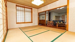 A tatami mat room with a sliding door leading to a living area, a wooden ceiling, and a traditional Japanese aesthetic. - Agari (Ie)