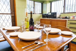 A dining table set with plates, wine glasses, and cutlery, with a bottle of wine and a microwave in the background. - Agari (Ie)