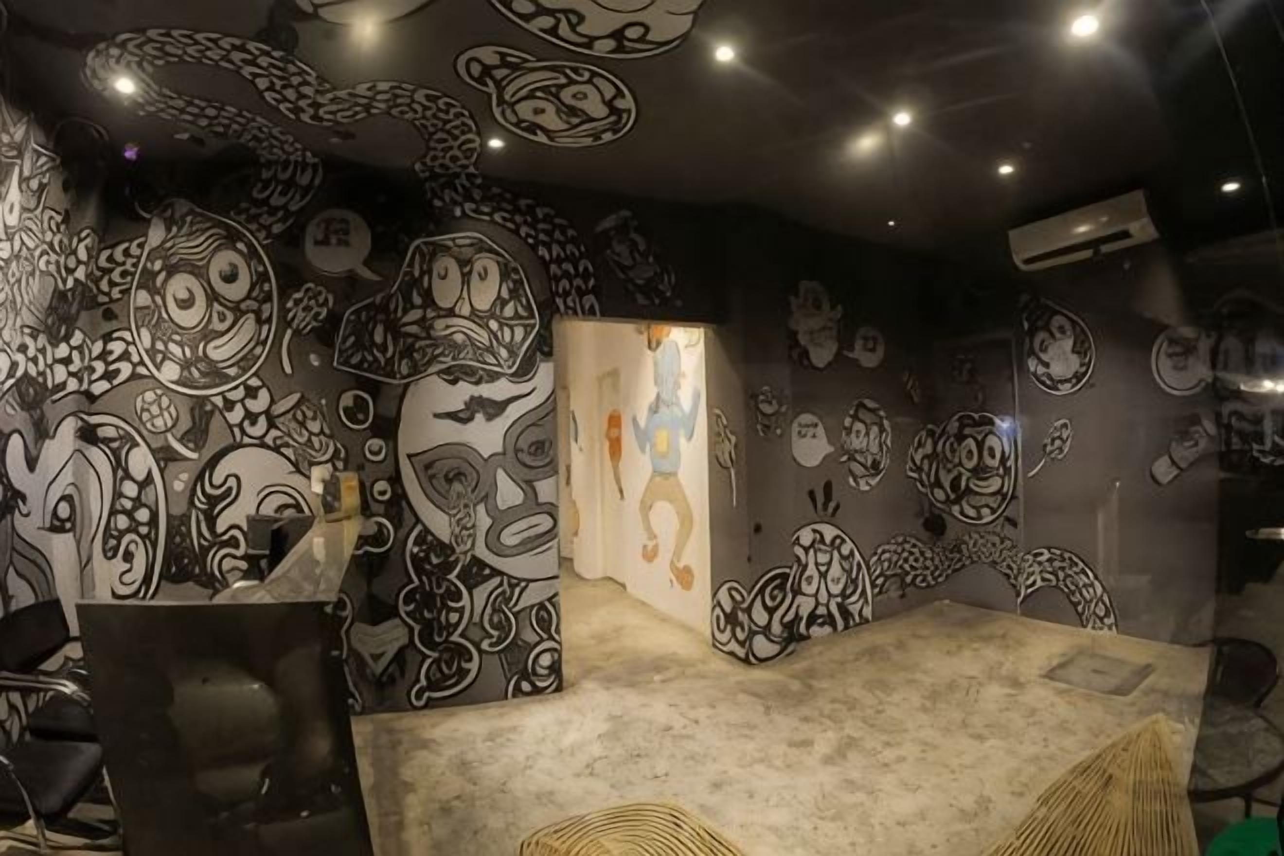 A room with a large, abstract mural on the walls, a small table, and a chair.