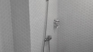 A shower with a hexagonal tile pattern on the walls and a metallic showerhead. - GRAB HOTEL GRESIK (Gresik)