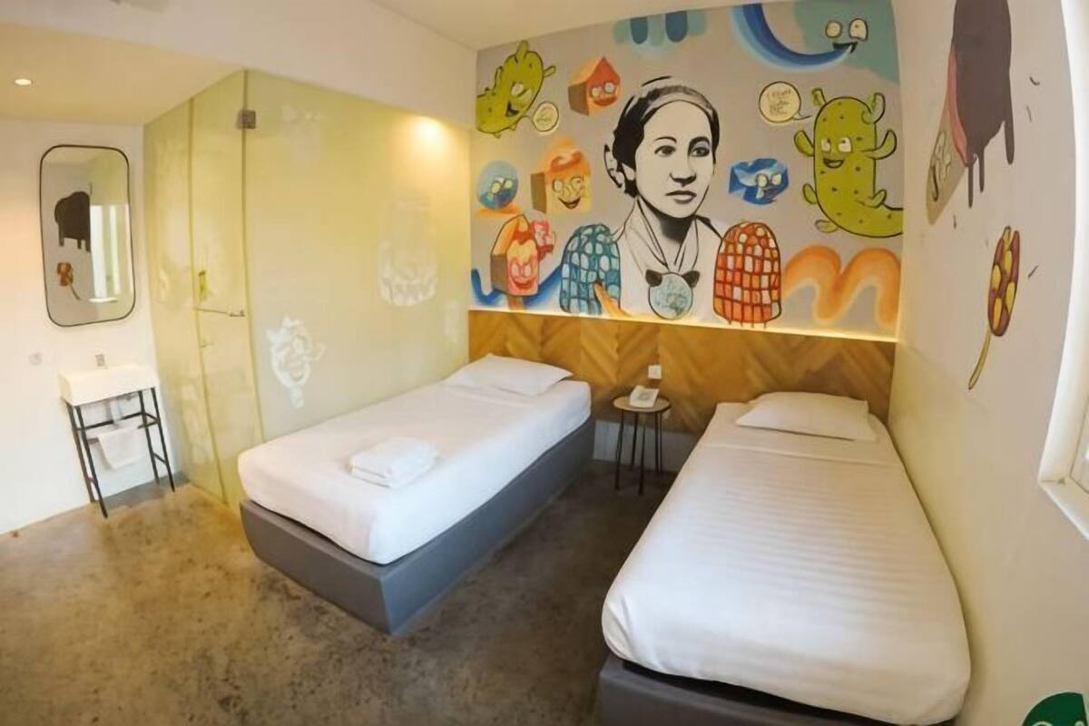 A room with two beds, a small table, a mirror, and a wall with colorful cartoon characters.