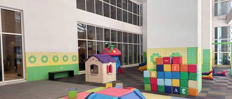 Zona infantil con un tobogán, bloques de espuma y una casita.