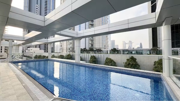 A modern indoor swimming pool with clear glass walls, surrounded by a minimalist architectural design and a view of city buildings. - Vogue | Mon Reve near Dubai Mall | Burj Khailfa (Dubai)