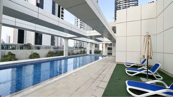 Un área de piscina interior moderna con agua azul cristalina, rodeada por un solárium con baldosas y sillones de descanso.