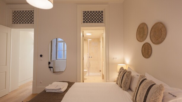 A hotel room with a bed, a bathroom visible through an open door, and a mirror on the wall. - Nomad's Lisbon Call 2BDR Rua Augusta (Lisbon)