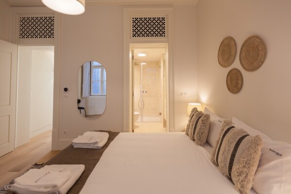 A hotel room with a bed, a bathroom visible through an open door, and a mirror on the wall. - Nomad's Lisbon Call 2BDR Rua Augusta (Lisbon)