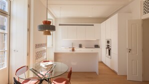 A modern kitchen with a central island, white cabinetry, and a glass dining table with chairs. - Nomad's Lisbon Call 2BDR Rua Augusta (Lisbon)