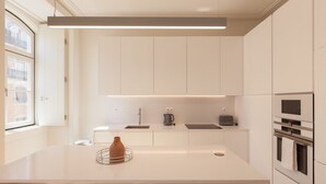 A modern kitchen with white cabinetry, a central island, a built-in oven, and a window providing natural light. - Nomad's Lisbon Call 2BDR Rua Augusta (Lisbon)