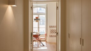 A hallway with wooden flooring leading to a dining area with a table and chairs. There is a door on the right and a light fixture on the left. - Nomad's Lisbon Call 2BDR Rua Augusta (Lisbon)