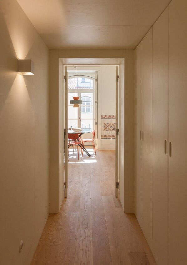 Een gang met houten vloer die uitkomt in een eetgedeelte met een tafel en stoelen. Aan de rechterkant zit een deur en aan de linkerkant een lamp.