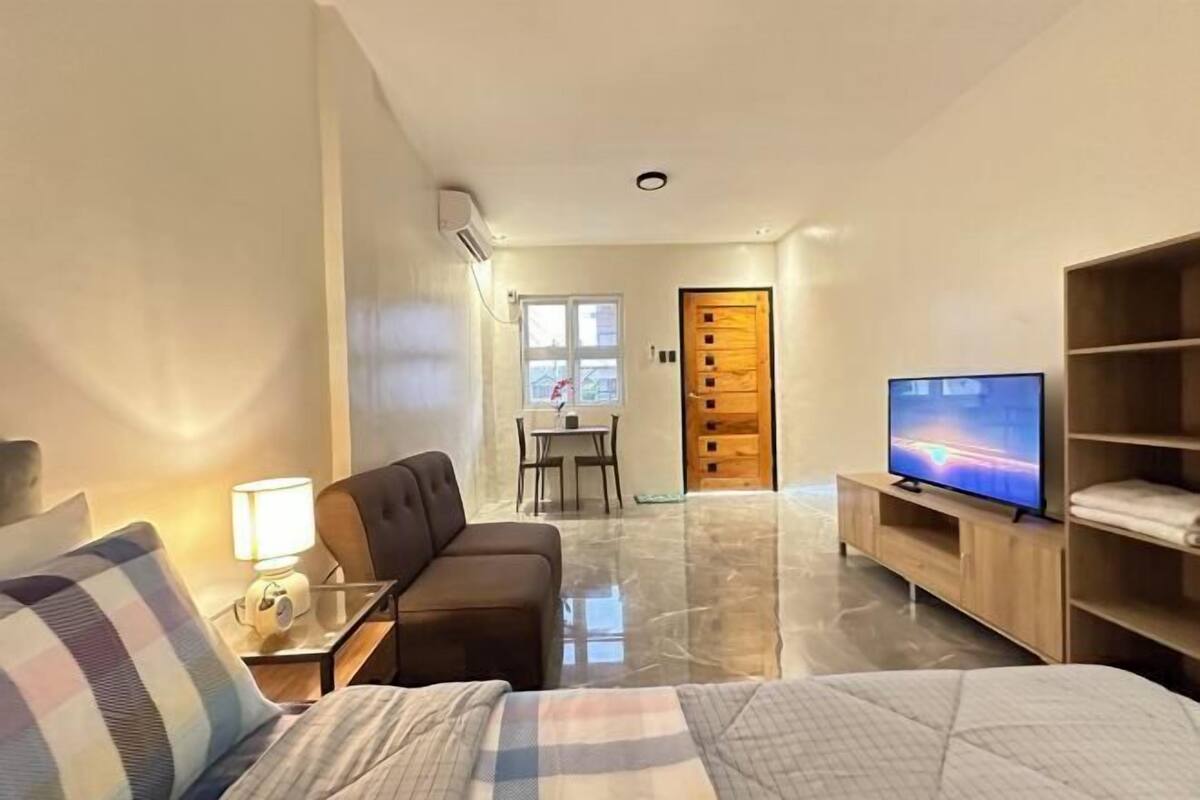 A hotel room with a bed, a sofa, a TV, a wooden door, and a small table with a lamp.