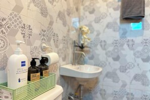 A bathroom with patterned tiles, a sink, and toiletries in a green basket. - F Residence Transient House (Nueva Ecija)