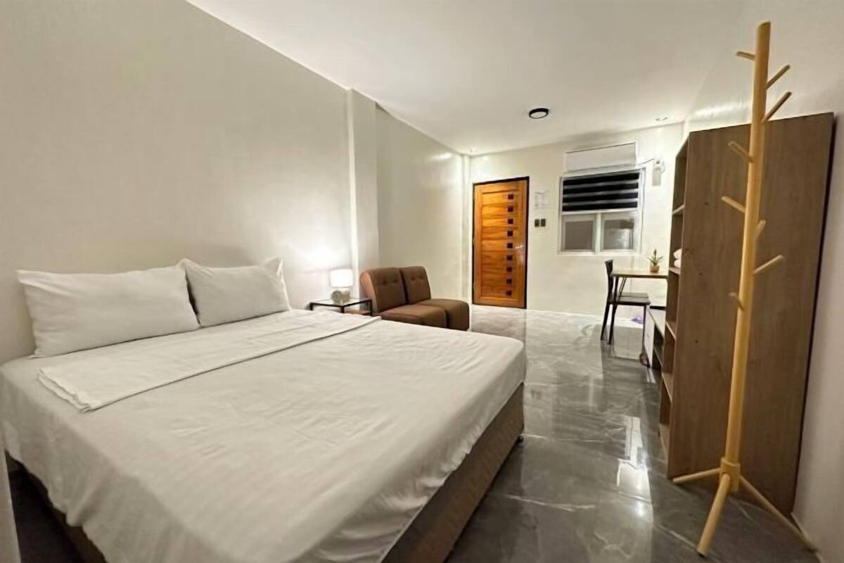 A bedroom with a bed, a wooden wardrobe, a small table, and a chair.