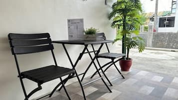A patio area with two black metal chairs and a small table, a potted plant, and a menu stand.