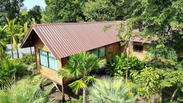 A wooden cabin with a sloped roof, surrounded by dense tropical vegetation.