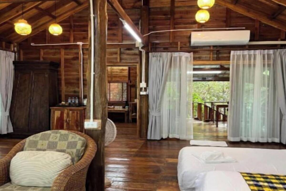 A wooden cabin interior with a bed, wicker chair, and a dining area.