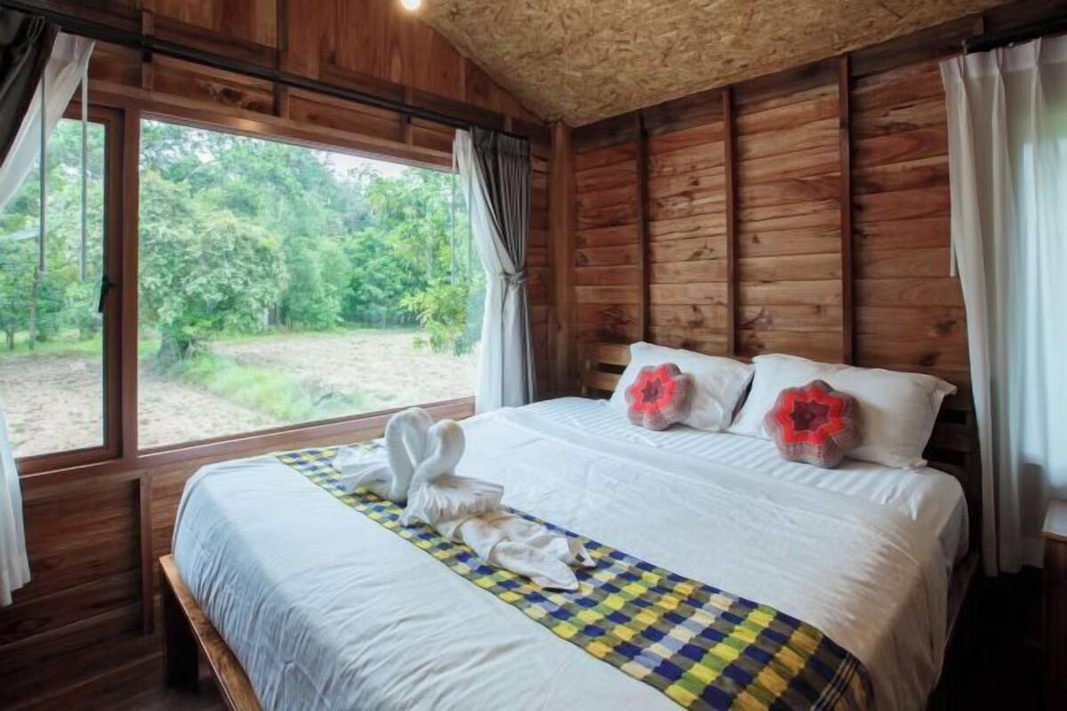 Een houten slaapkamer met een groot bed, uitzicht op de natuur en een raam met gordijnen.