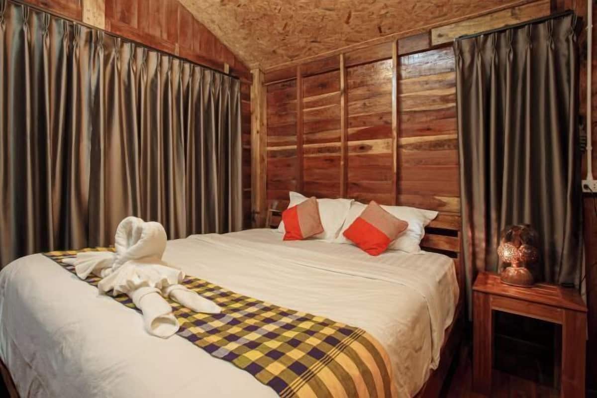 Een kamer met houten lambrisering, een bed, gordijnen en een klein tafeltje met een vaas.