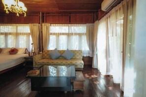 Una habitación con una cama, un sofá con cojines, una mesa de centro de vidrio y una ventana con cortinas.