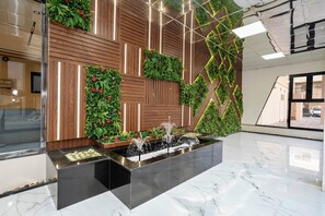 A modern lobby with a marble floor, wooden paneling, green vertical gardens, and a water feature. - Taj Al Munira Serviced Apartments (Dammam)